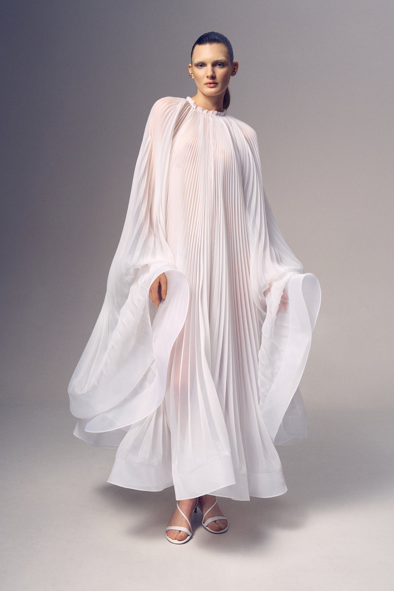 Virgin Dress by J'amemme — model in white pleated bridal gown showing ethereal flowing silhouette, studio full-body shot